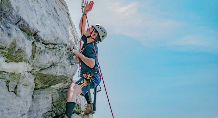 A person wearing safety gear is secured by ropes while rock climbing against a blue sky. 